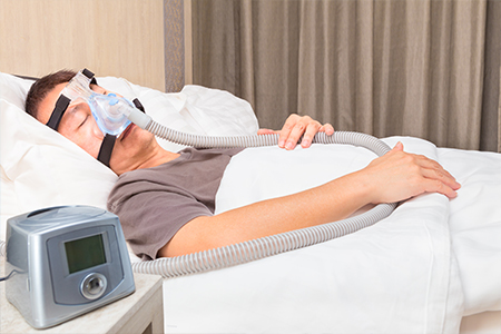 Middle age asian man sleeping in his bed wearing CPAP mask connecting to air hose and CPAP machine, device for people with sleep apnea