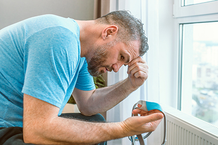 Unhappy shocked man with chronic breathing issues surprised by using CPAP machine sitting on the bed in bedroom. Healthcare, CPAP, Obstructive sleep apnea therapy, snoring concept