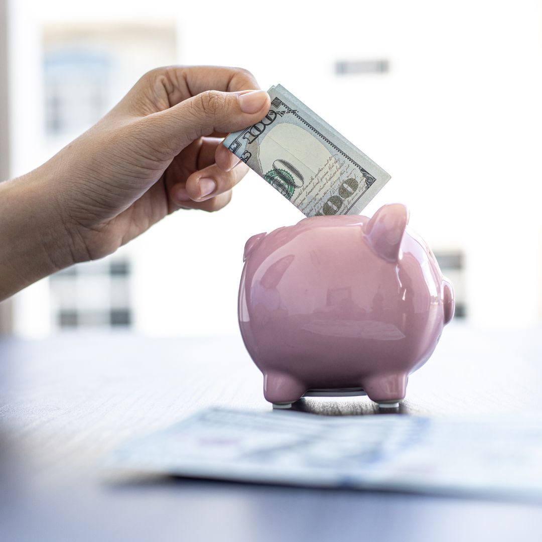 a person putting a one hundred dollar bill in a piggy bank