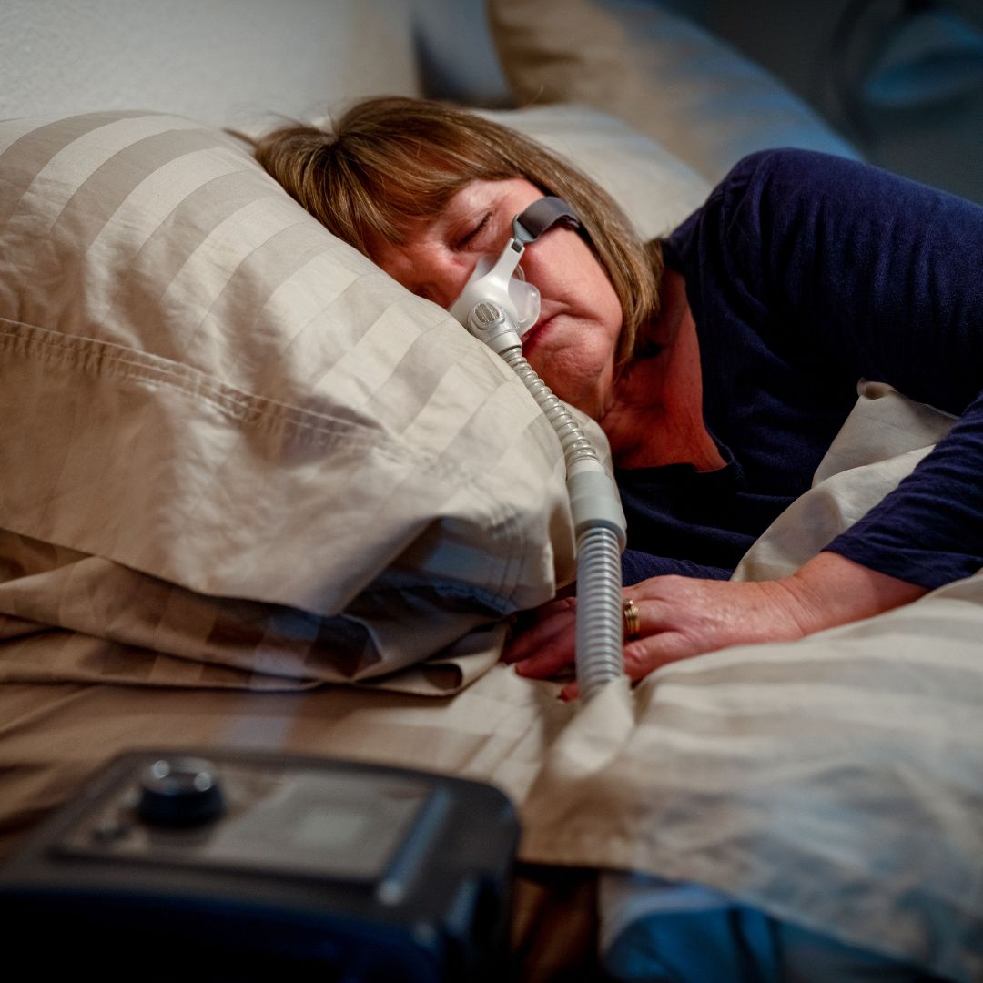 a woman sleeping in bed wearing a CPAP machine