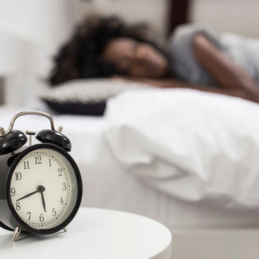 a clock next to a sleeping woman in bed